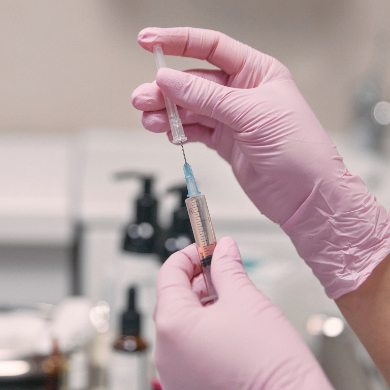 Practitioner in pink gloves preparing a syringe for treatment